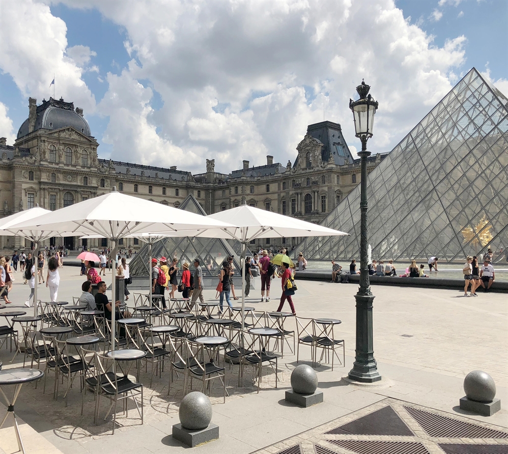 A series of center pole umbrellas with white fabric on a patio next to the louvre in paris