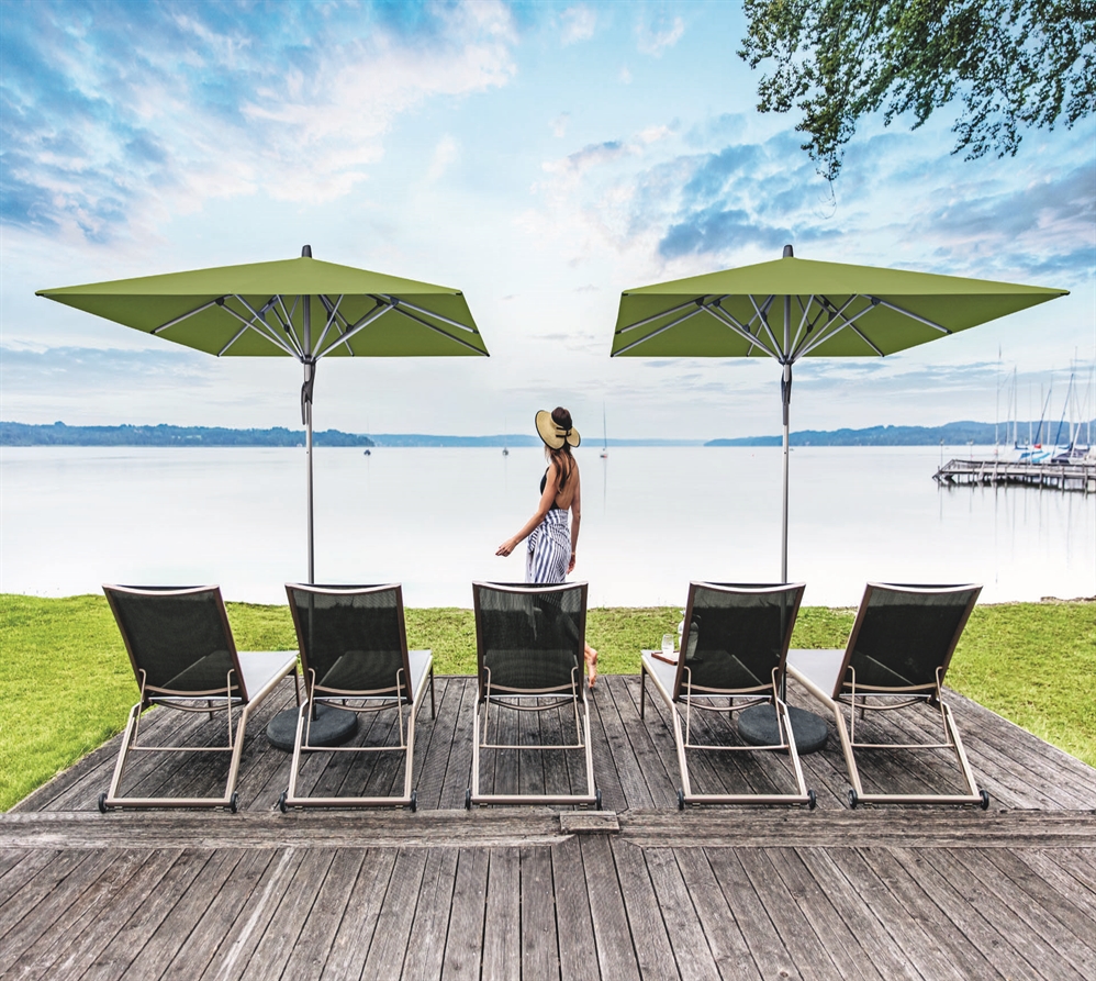 A small oceanside patio with 2 green umbrellas covering the patio furniture, overlooking the ocean