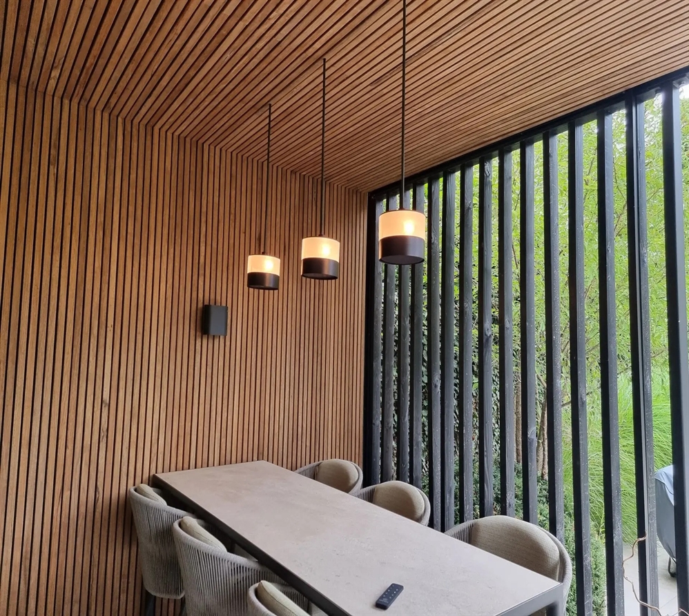 Three pendant lights hanging above a modern dining table in a wooden slatted outdoor patio.