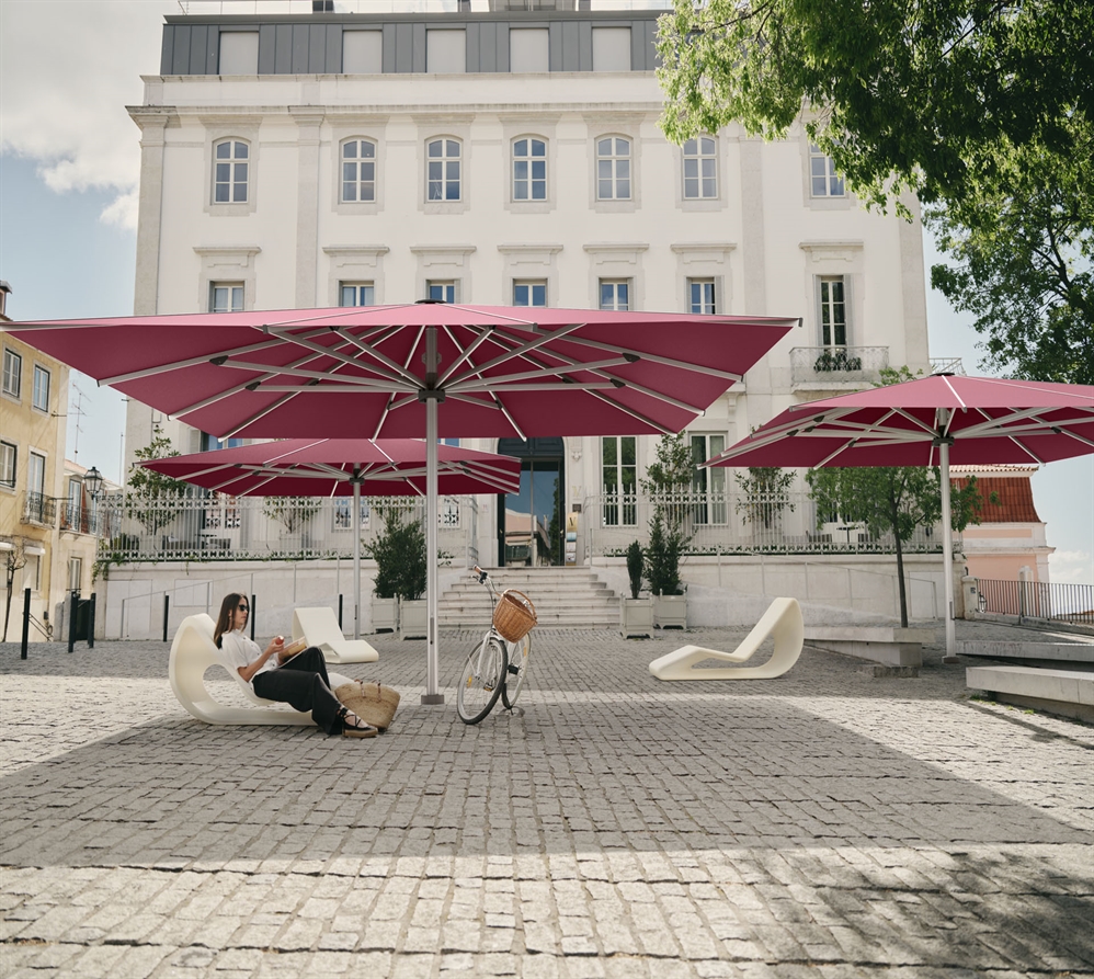 A lady sitting under one of three giant pink umbrellas in a public courtyard