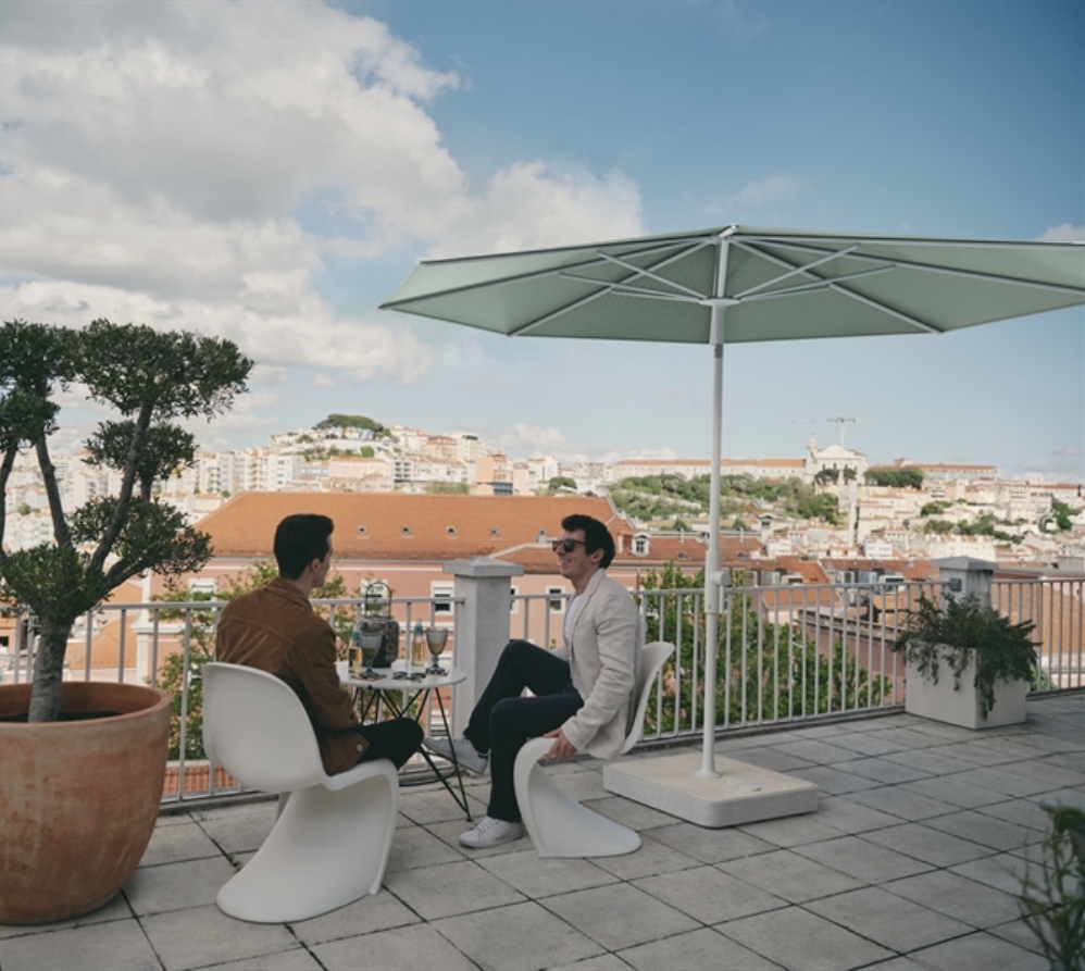 2 people sitting on an above ground patio underneath an umbrella with light green fabric