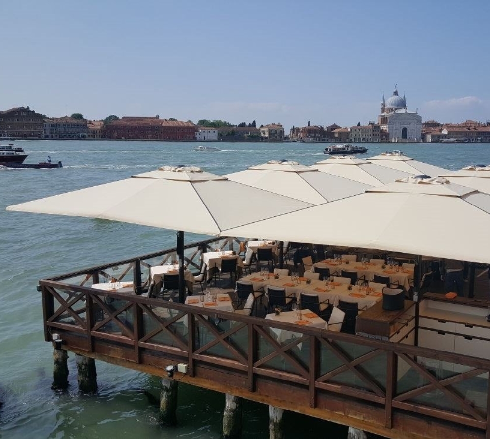 a series of 8 big beige patio umbrella on a patio deck over the water with tables and chairs under a series of 8 big beige patio umbrella on a patio deck over the water with tables and chairs under