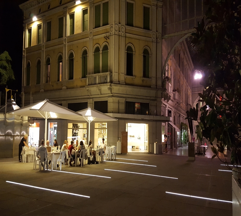 large white umbrella with backlit panels in the night time covering a restaurant patio 