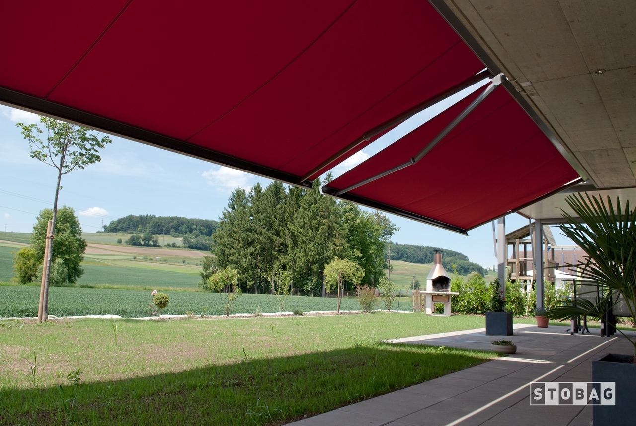 Two large red arm bracket awning shade a backyard patio