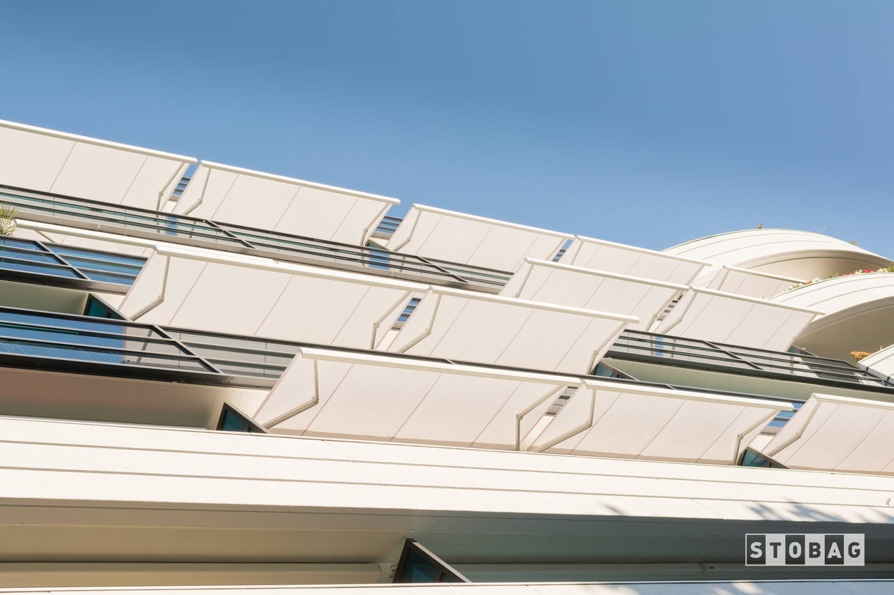 Underside view of several white arm bracket awnings over apartment patios