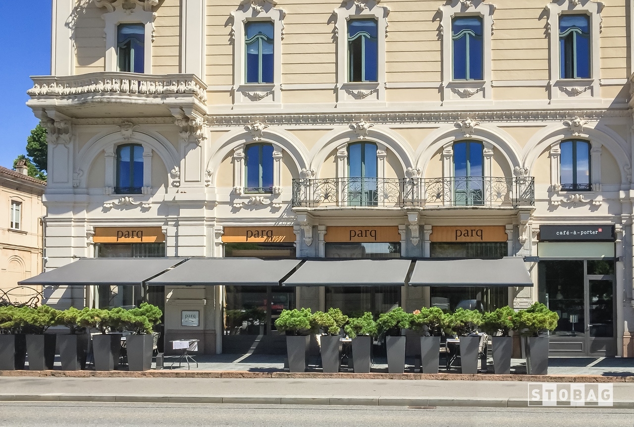 Four grey arm bracket awnings open and shading a restaurant patio