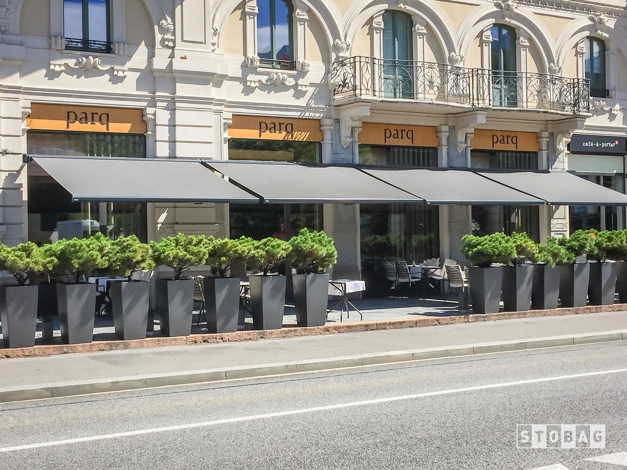 Four grey arm bracket awnings open and shading a restaurant patio