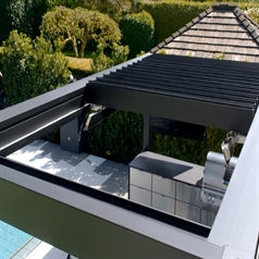 black louvred pergola with louvres open attached to the facade of a home covering the patio