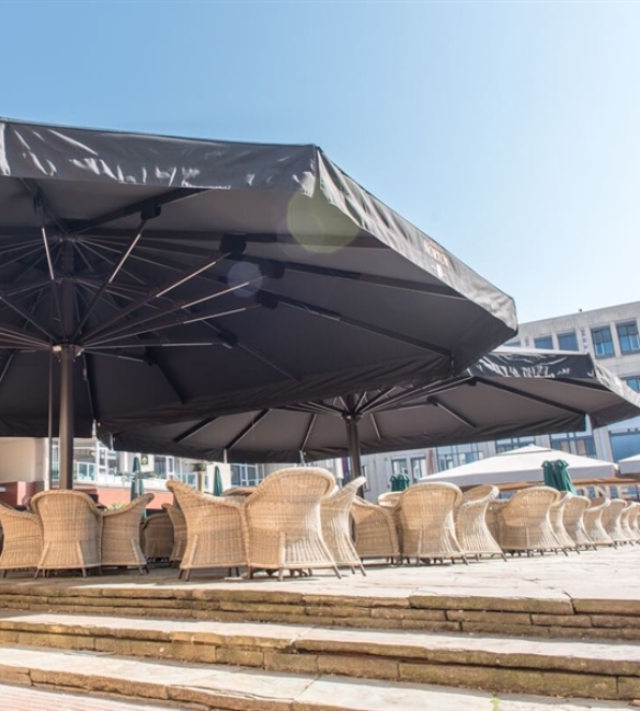 Two extra large black Golia parasols over an outdoor café seating area