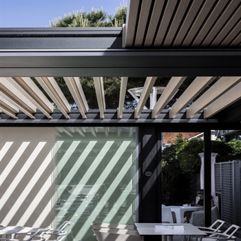 Restaurant patio with black aluminum pergola with wood finish louvers retracted and tilted