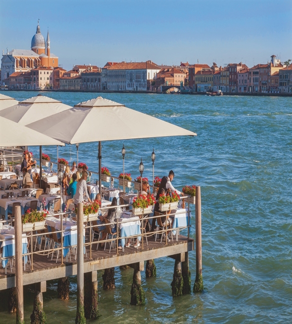 restaurant patio on top of the water overlooking the water and city ahead with beige umbrellas open