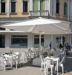 small outdoor patio in daytime with large patio umbrellas and white chairs and tables underneath