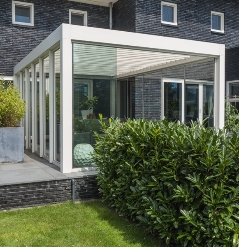Sliding glass panels enclose the sides of an aluminum louvered pergola over a patio living space