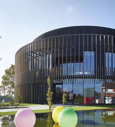 Vertical louvers in bronze providing shade to a circular building with floor to roof glass windows