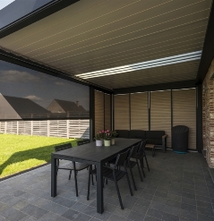Retractable louvered pergola over an outdoor patio with light shining thru glass translucent blades