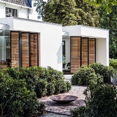 black aluminum panels with brown wooden louvres folded against the facade of a white home