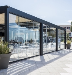 Freestanding aluminum louvered black pergola with integrated glass panel walls over an outdoor patio