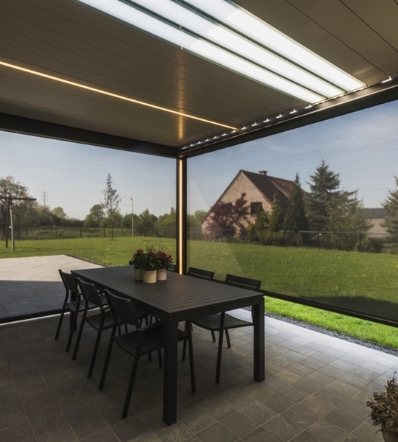 Light shines through the translucent glass louvres of an aluminum pergola over a patio 