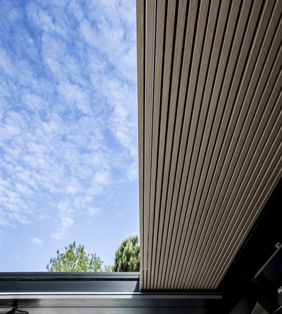 Aluminum wood finish louvers of a pergola shown up close in a retracted position with blue sky