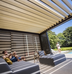 a family sitting underneath a louvred canopy with beige louvres and a brown frame poolside in sun