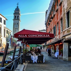 Red side arm logoed parasol along canal over patio diners