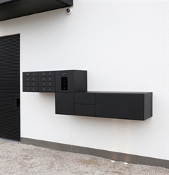 black aluminum mailboxes elevated from the ground installed in the middle of a white wall