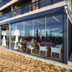 Sliding glass panels enclose an outdoor restaurant patio providing protection from the elements