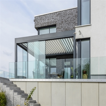 Sliding glass panels enclose the sides of an aluminum louvered pergola over a patio living space