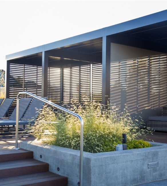 Loggia metal panels with wood finish slats that tilt and retract on a pergola 