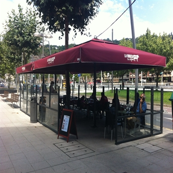 a street side enclosed restaurant patio covered with red branded patio umbrellas and people dining