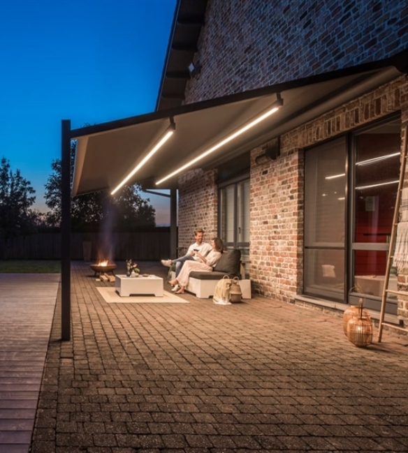 Light beams under a PVC retractable pergola with couple enjoying their outdoor space at night