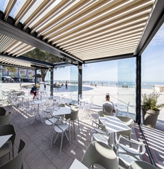 Outdoor restaurant patio covered with a aluminum pergola and wood finish louvers tilted oceanside