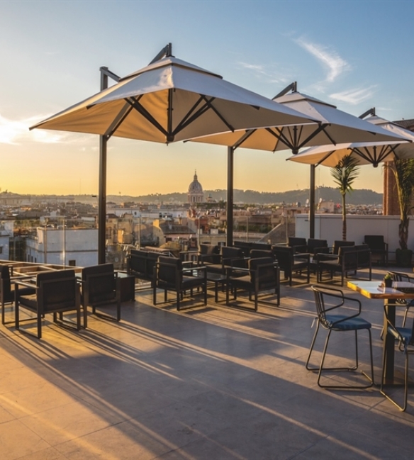 Three cream parasols above a rooftop restaurant patio seating overlooking the city below