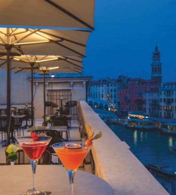 Backlit parasols over a patio along the canal at night with two martinis on the table