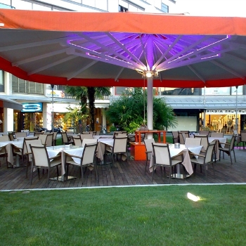 Large Golia orange parasol with lighting underneath over an outdoor restaurant dining area