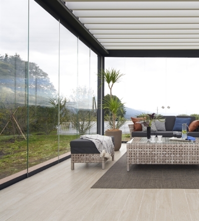 Sliding glass panels enclose the sides of an aluminum louvered pergola over a patio living space