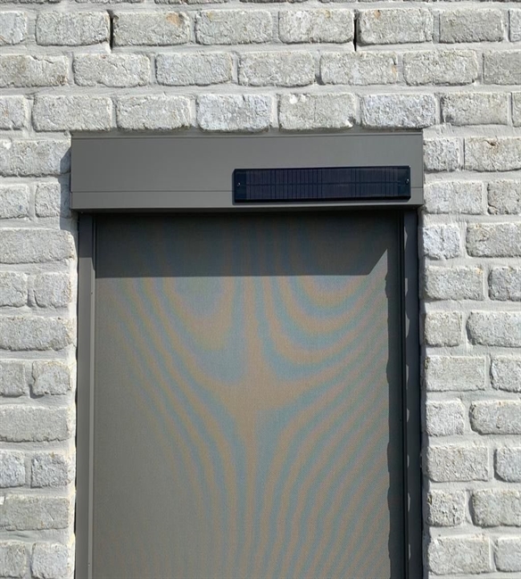 close up of a grey solar powered screen on a grey brick building with grey fabric fully extended