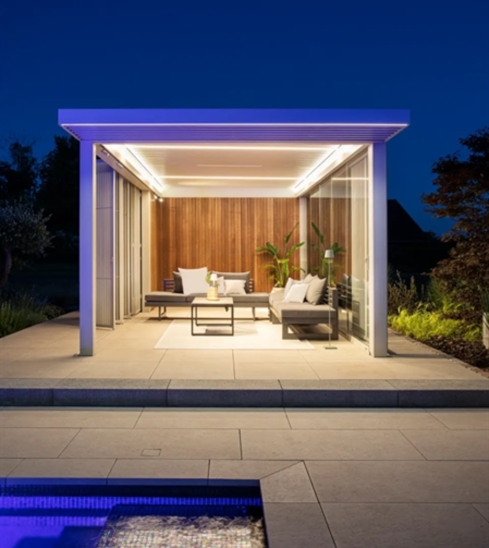 Modern pergola with wood slats by infinity pool, outdoor sofa reflected in water at sunset.