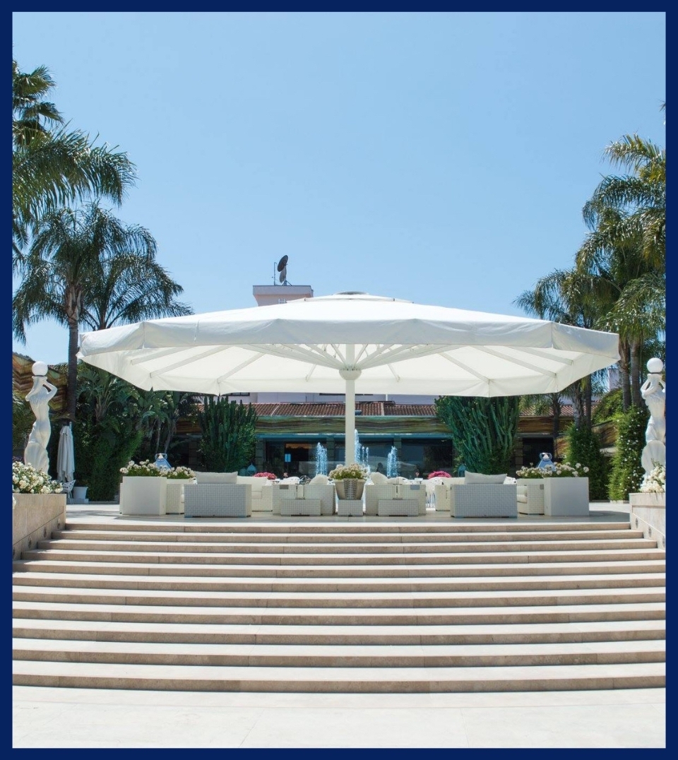 large white outdoor umbrella covering a very large patio space with white seating chairs underneath