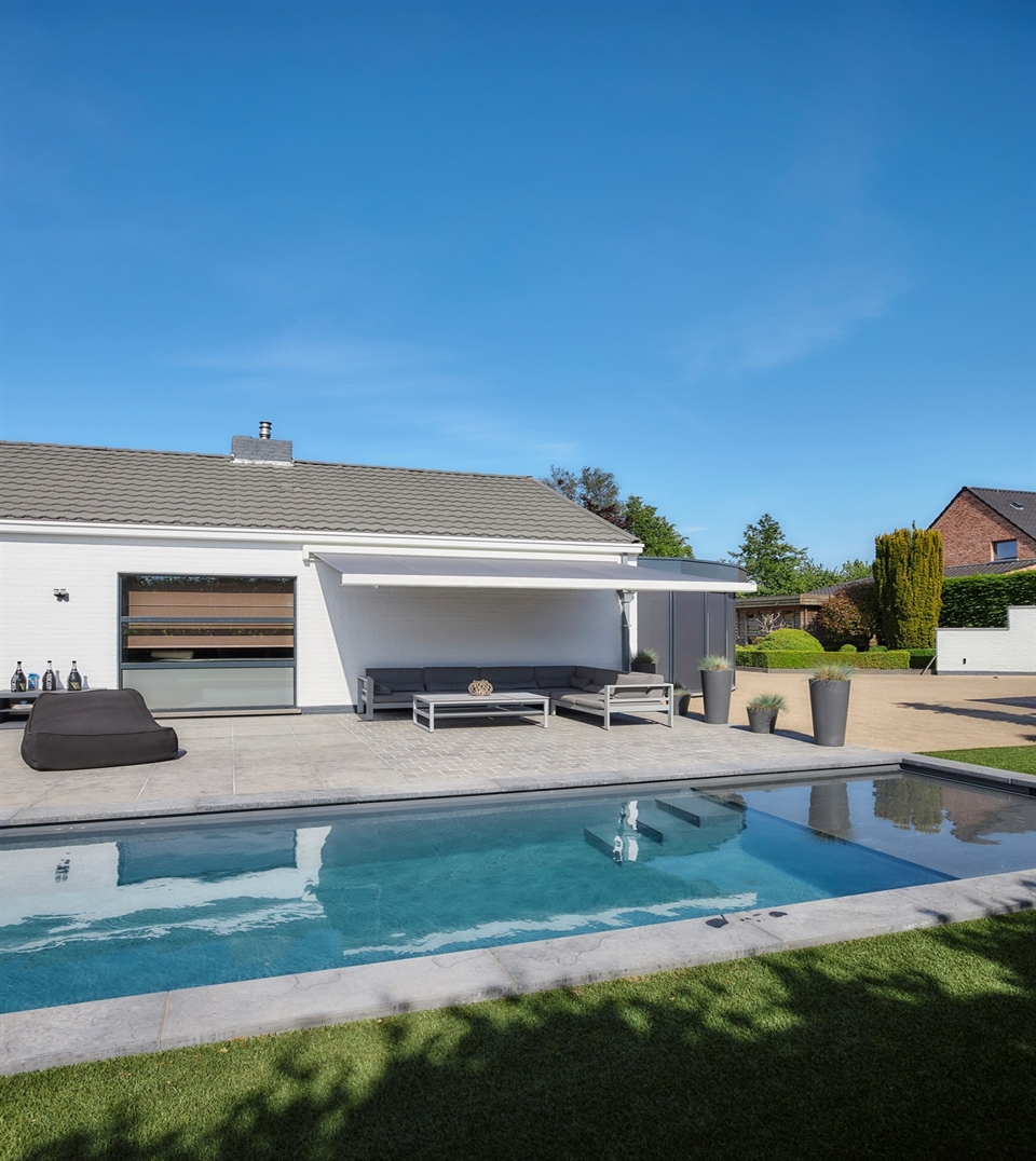 Modern backyard with a poolside lounge area shaded by a sleek retractable awning
