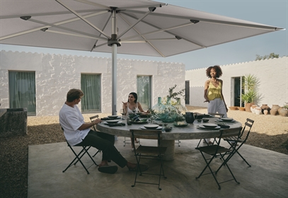 3 people sitting underneath a giant white umbrella chatting and dining