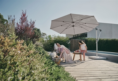 A white umbrella poolside with a family sitting underneath on a sunny day