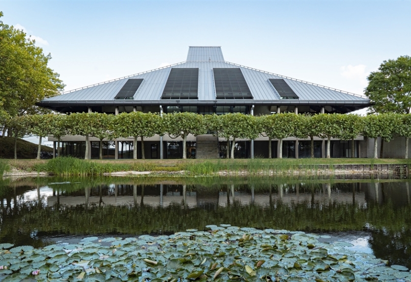 A pond sits in the foreground with a modern building in the background