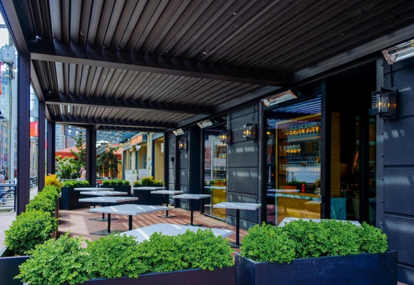 A metal pergola shades an outdoor restaurant patio