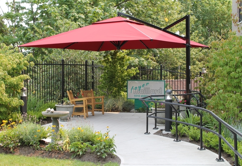 A red Gaggi Venezia patio umbrella shades a small seating area surrounded by gardens