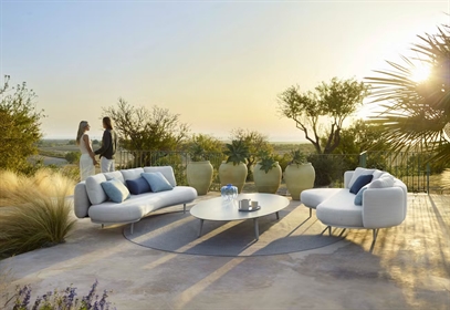 Modern outdoor lounge with curved white sofas, round table, and scenic sunset view.