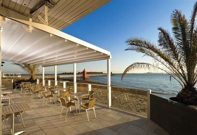 A white coloured retractable pergola on a restaurant patio wall mounted