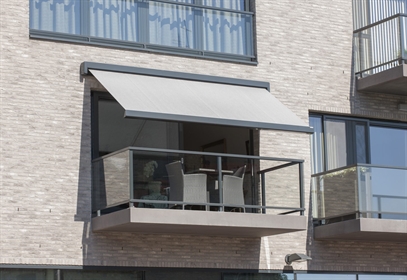 Modern balcony with glass railing and light gray retractable awning.