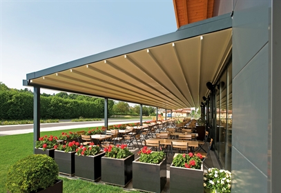 A large restaurant patio covered by a wall mounted retractable pergola