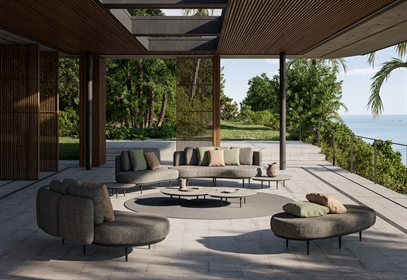 Contemporary outdoor lounge with modular dark sofas, round tables, and ocean view.